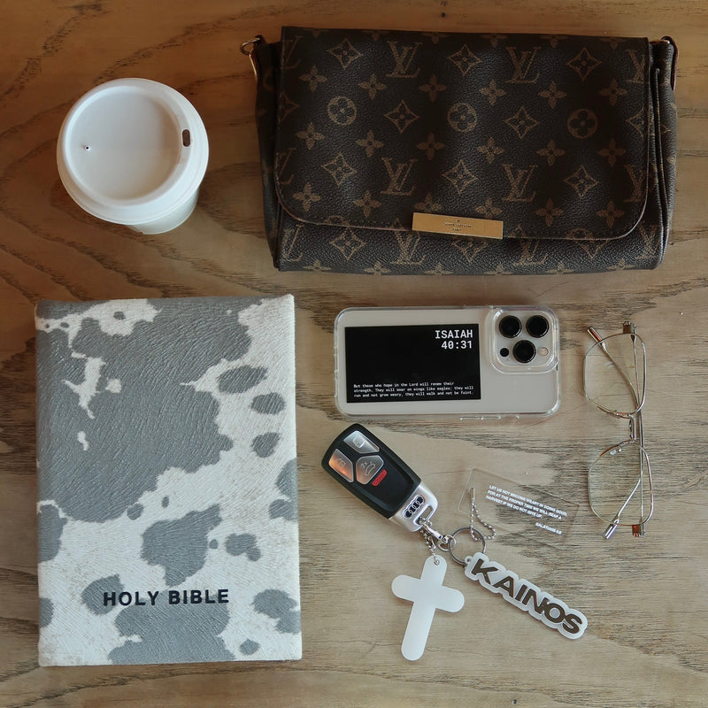 Collection of items including a Louis Vuitton wallet, phone, keychain, glasses, and a Holy Bible on a wooden surface.
